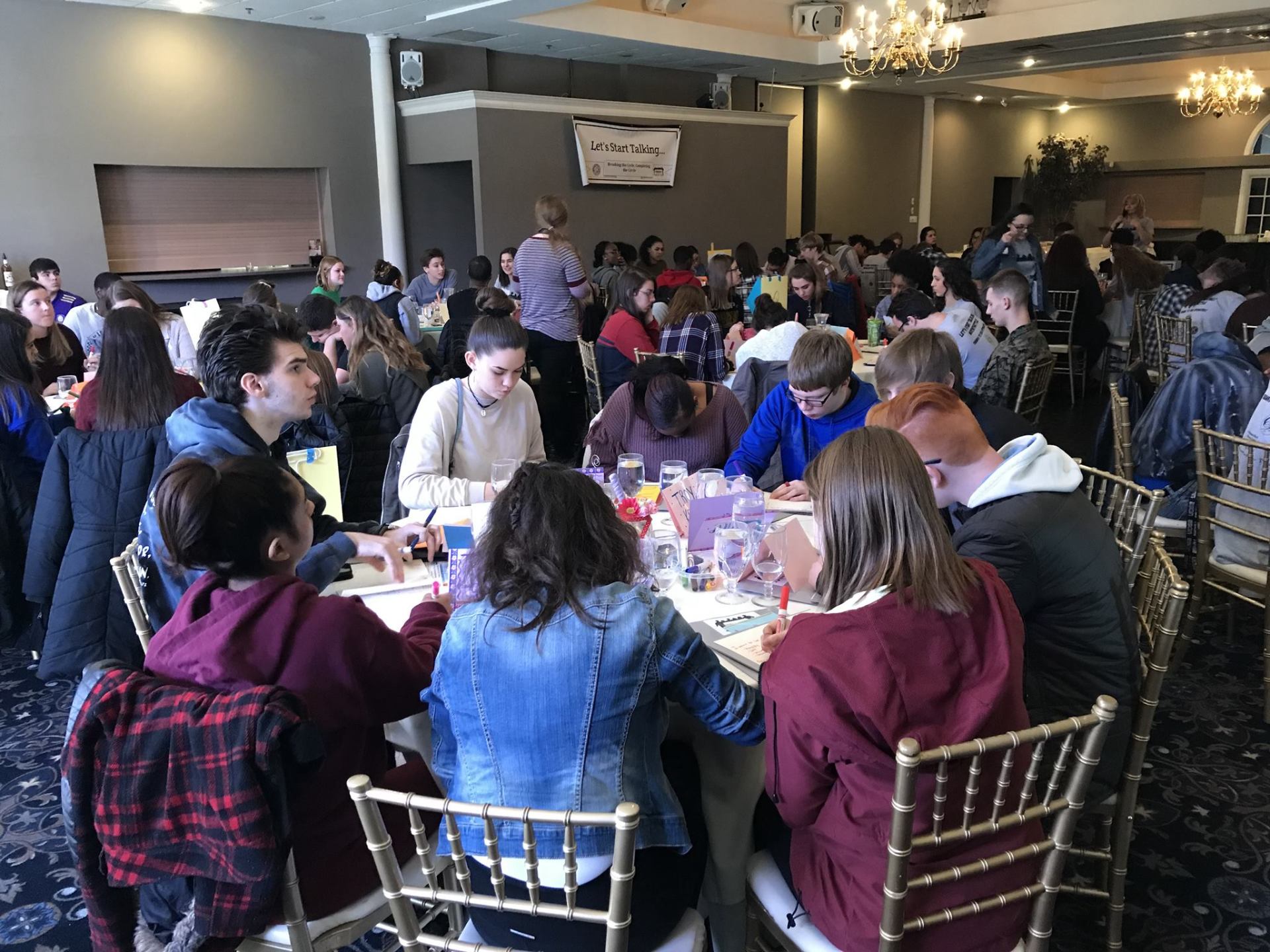 A large group of people are sitting at tables in a large room.