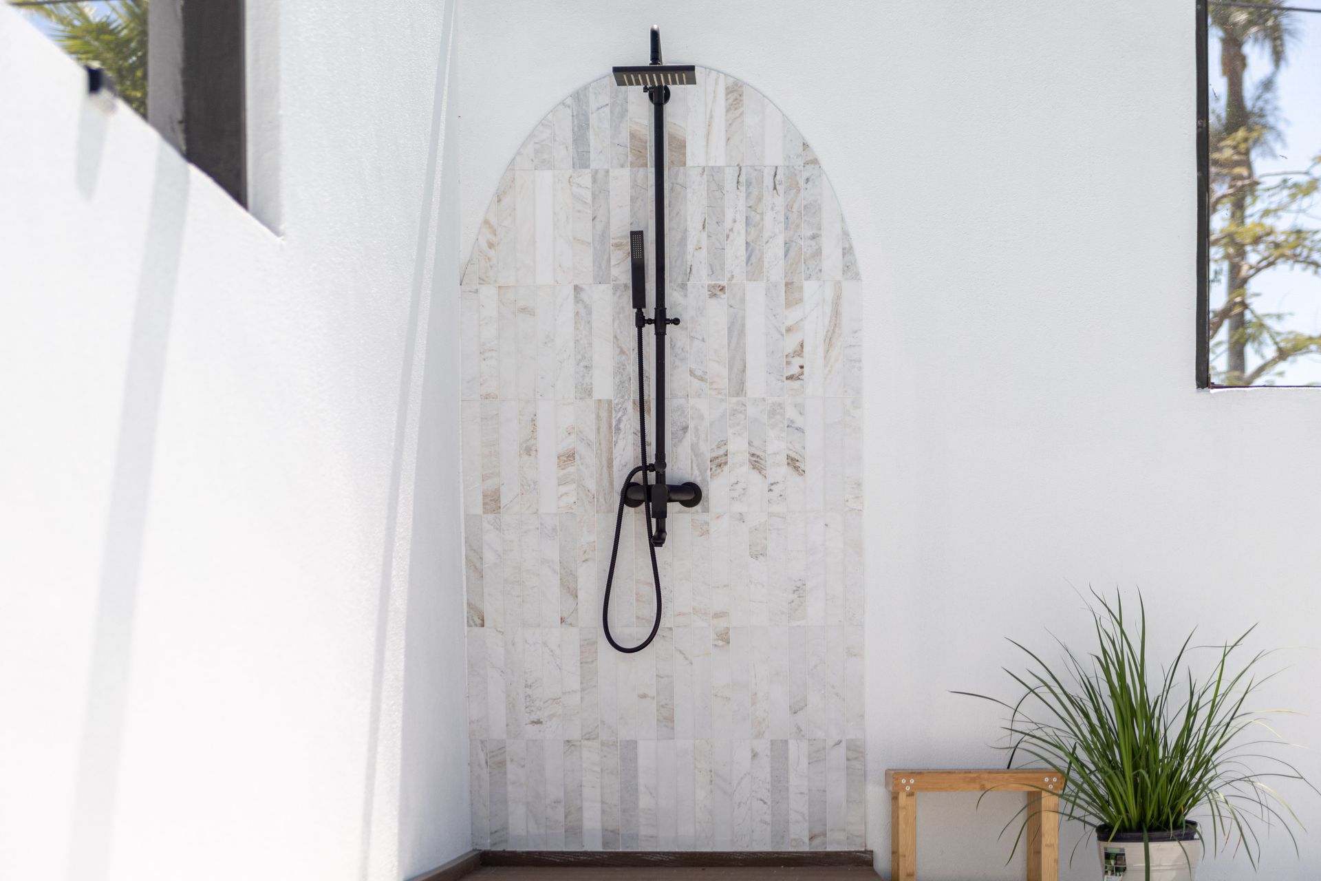 There is a shower with a black shower head hanging from the wall.