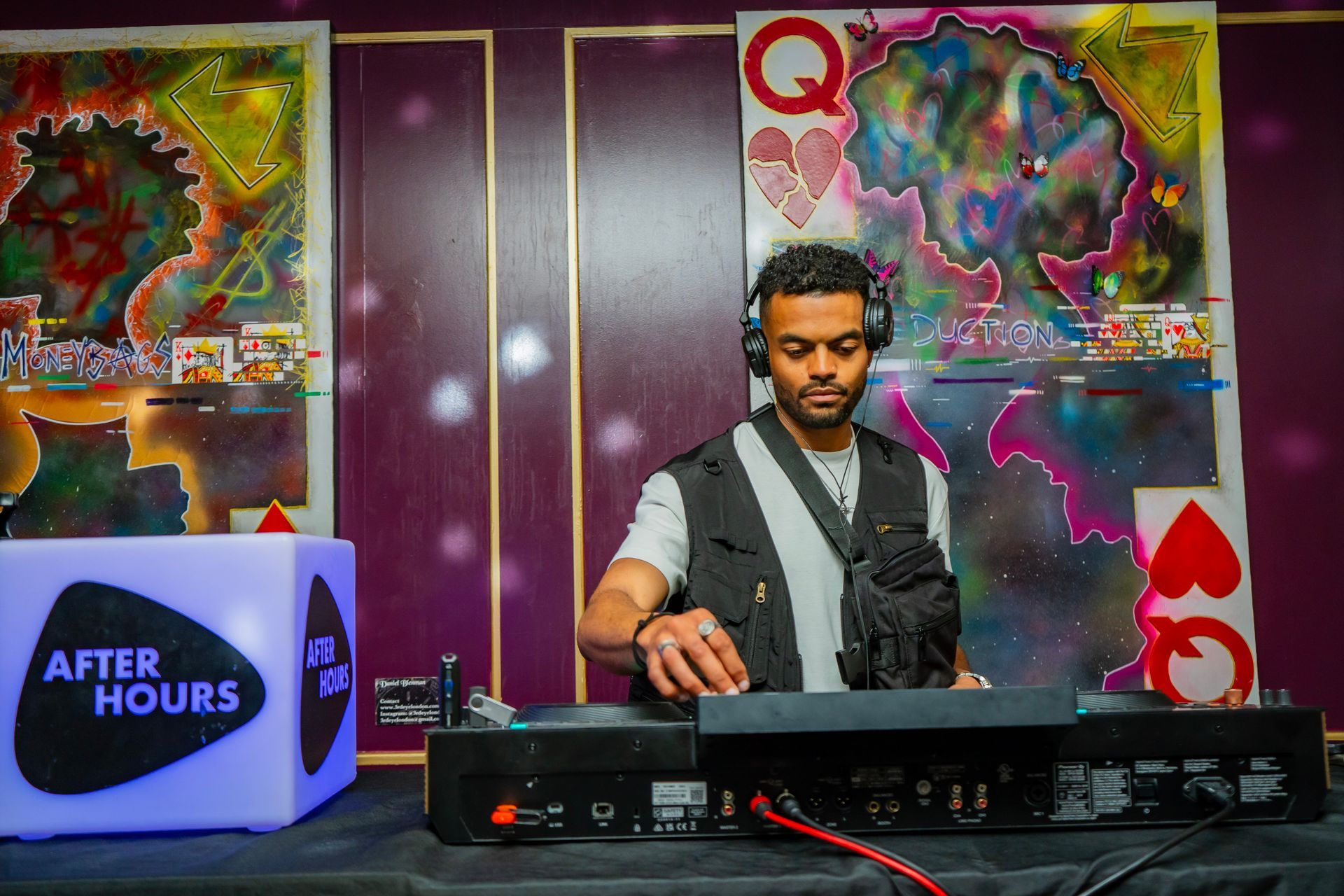 A man is playing a dj set in front of a queen of hearts painting.