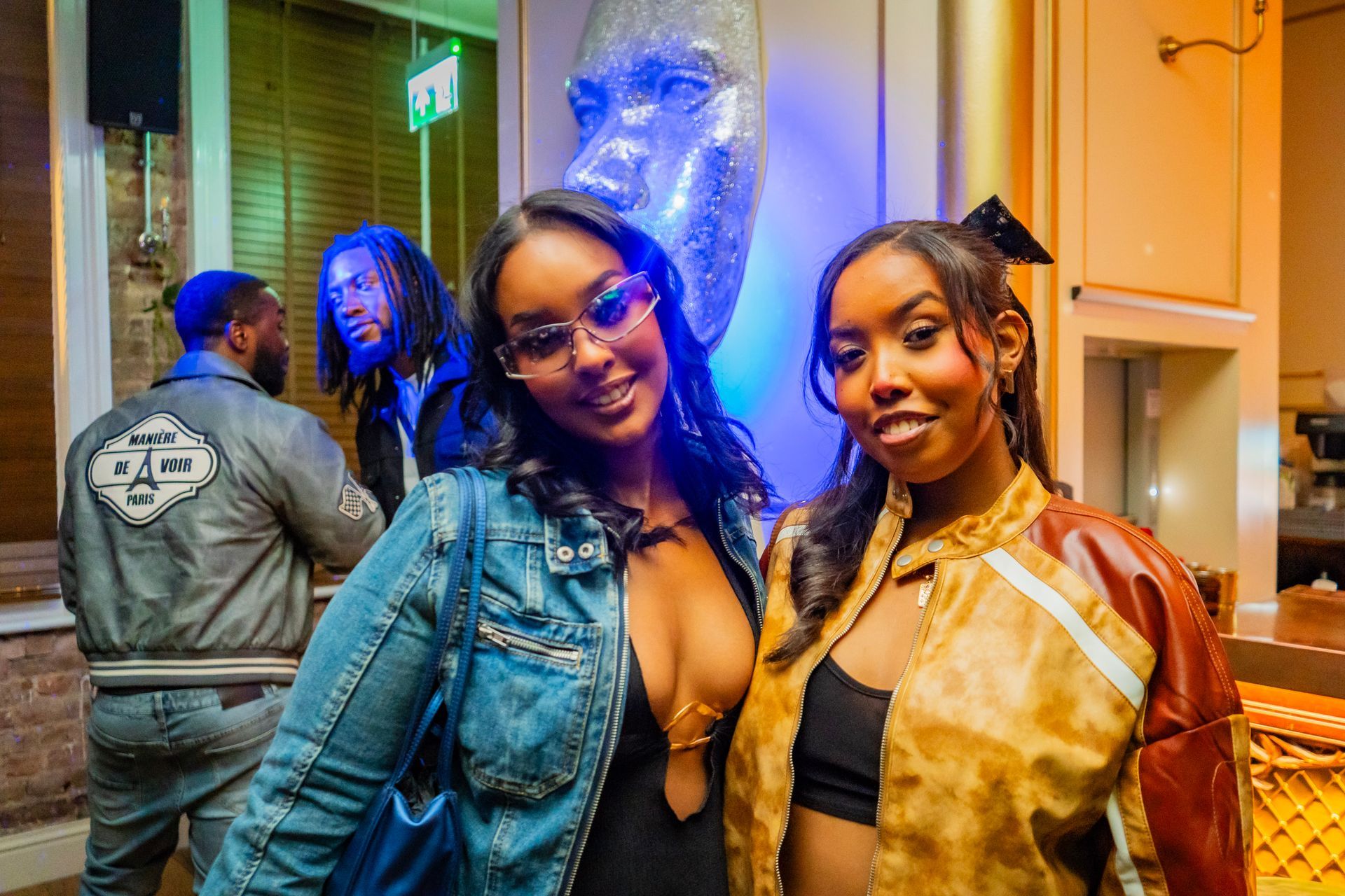 Two women are posing for a picture in a room with a man in the background.