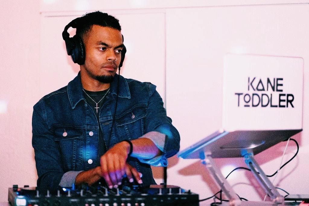 A man wearing headphones is playing music in front of a sign that says kane toddler.