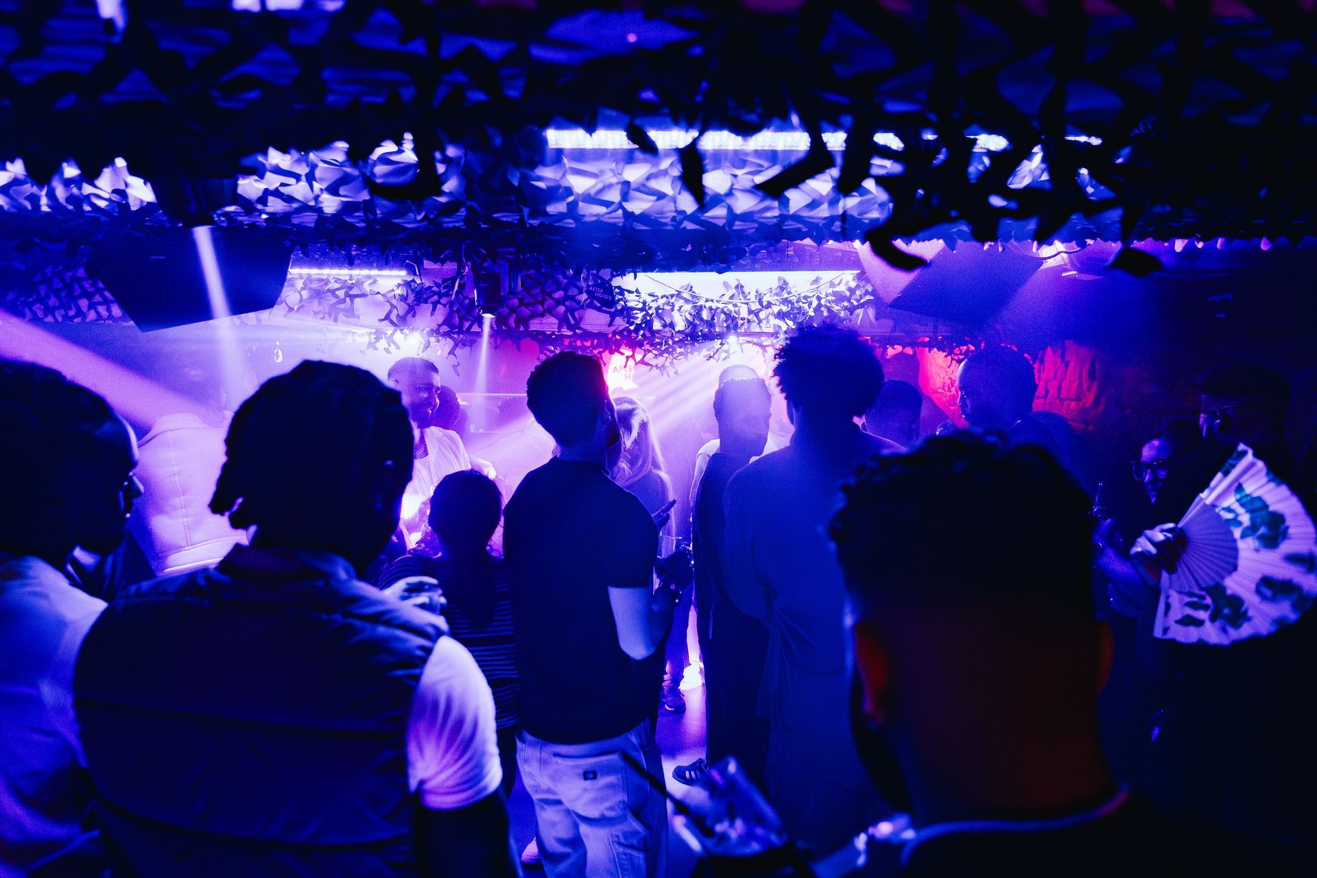 A group of people are dancing in a dark room with blue lights.