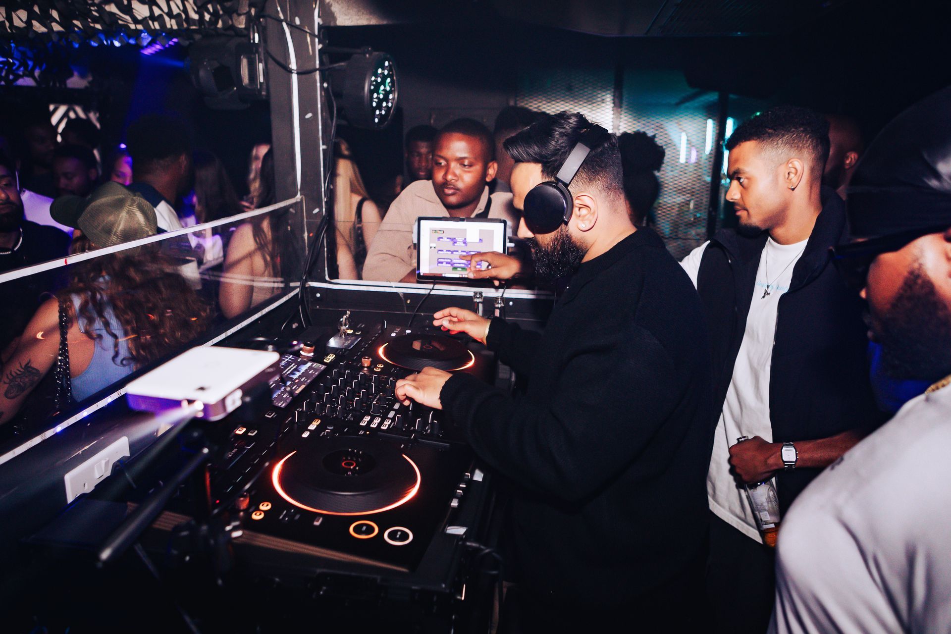 A group of people are standing around a dj at a party.