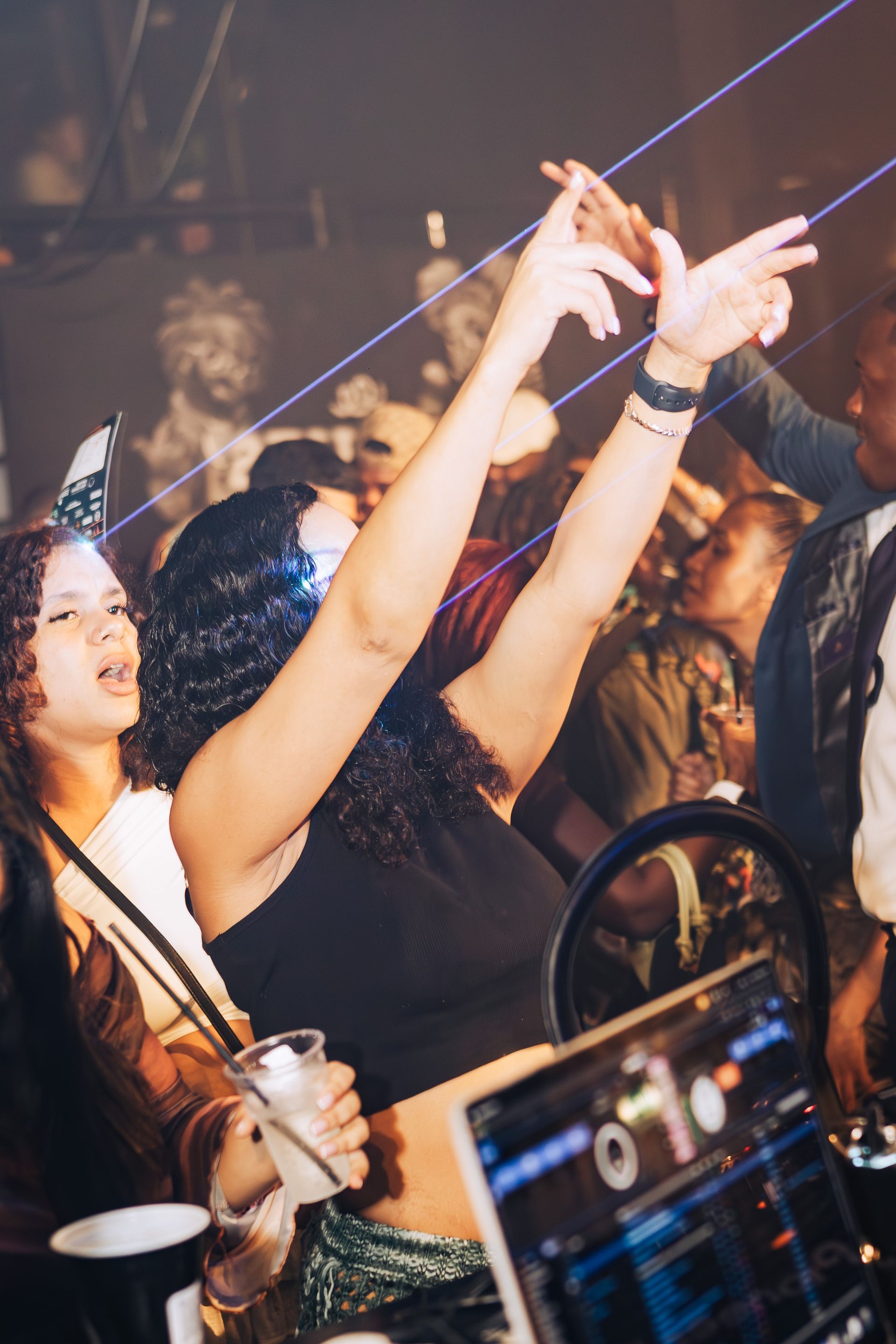 A group of people are dancing in a club with their arms in the air.