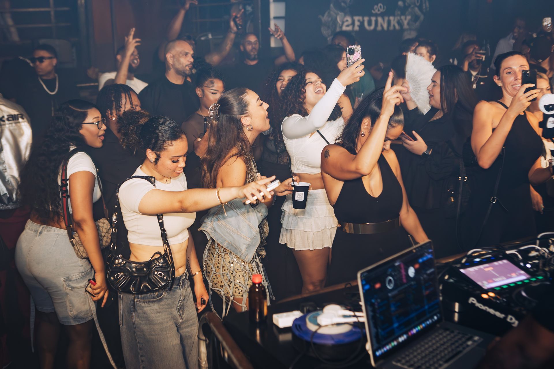 A group of people are standing around a dj booth at a party.