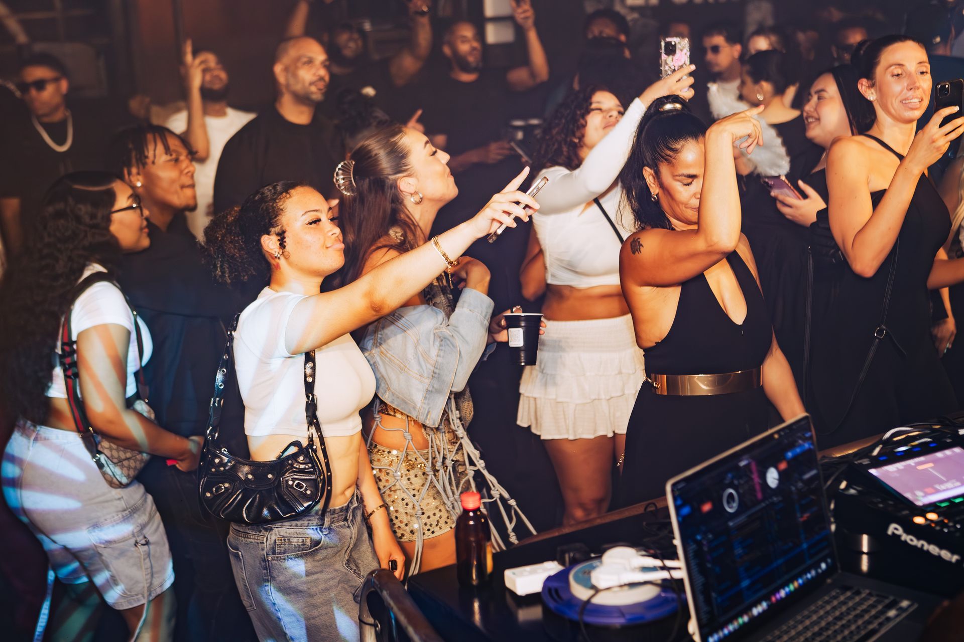 A group of people are standing around a dj booth at a party.