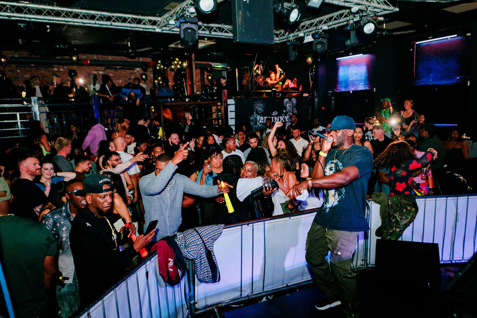 Man performs on stage at a crowded nightclub, audience cheering, flashing lights.