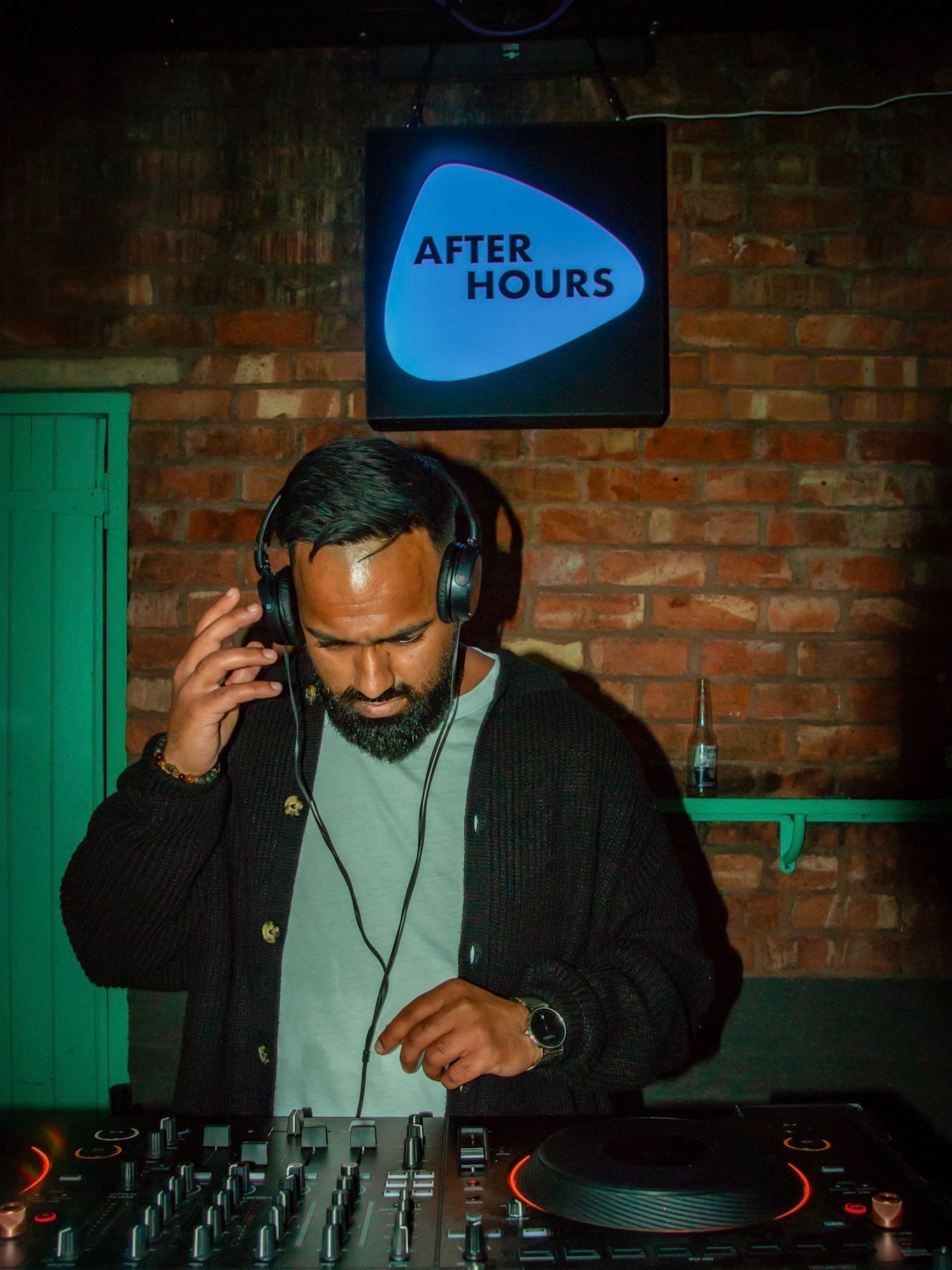 A man wearing headphones is playing music in front of a sign that says after hours.