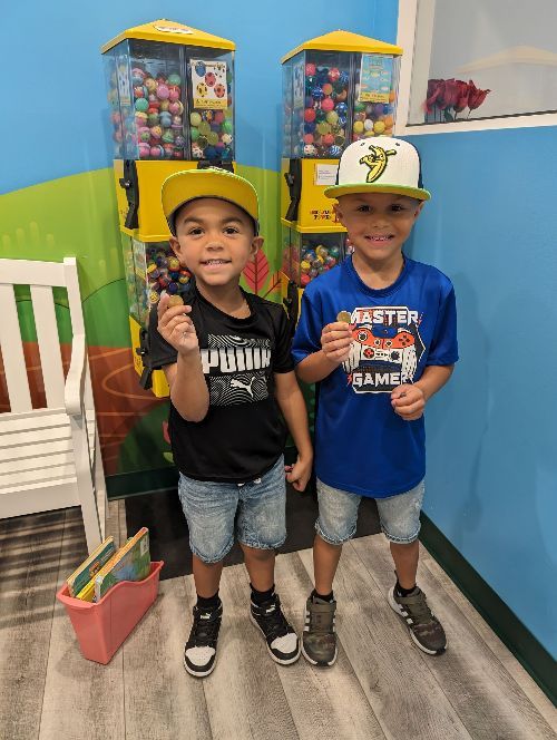 Two young boys are standing next to each other in front of gumball machines-Dental Studio 4 Kids-Lust FL