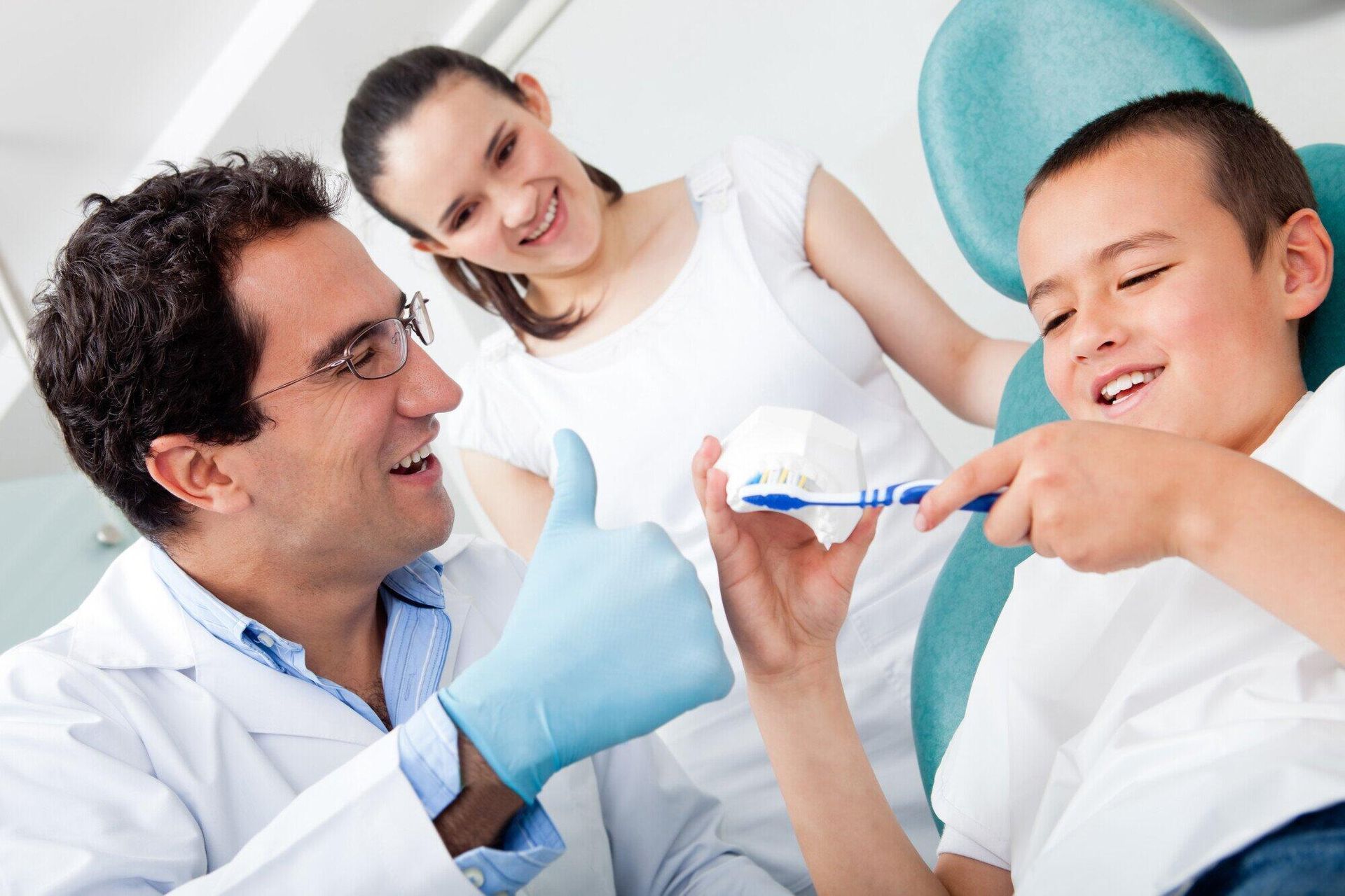 A dentist is giving a thumbs up to a young boy who is brushing his teeth