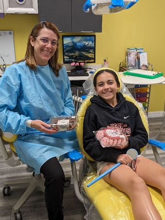 Dr. Denisse is sitting next to a girl in a dental chair holding a cake-Dental Studio 4 Kids-Lust FL