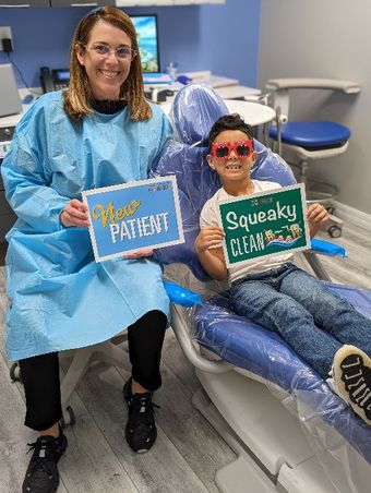 Dr. Denisse is sitting next to a boy in a dental chair holding signs- Dental Studio 4 Kids-Lust FL