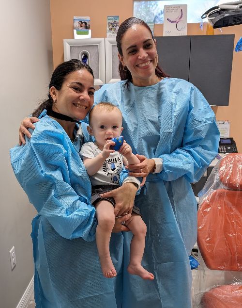 Two women are holding a baby in a dental office.