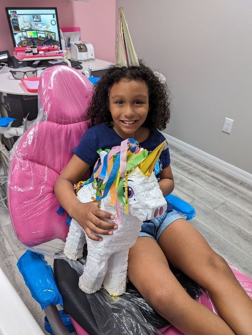 A little girl is sitting in a dental chair holding a unicorn piñata-Dental Studio 4 Kids-Lust FL