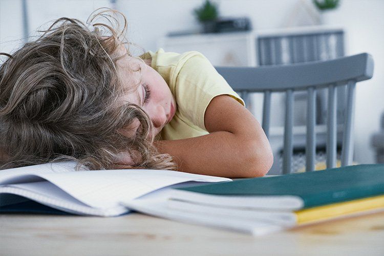 Young child sleeping with his head down on a school desk - Dental Studio 4 Kids