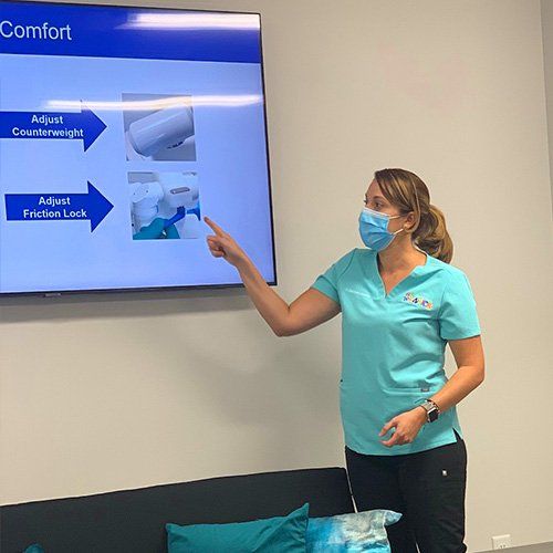 A woman wearing a mask is giving a presentation in front of a large screen.