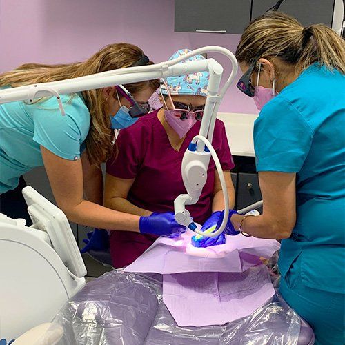 A group of female dentists are working on a patient 's teeth in a dental office.