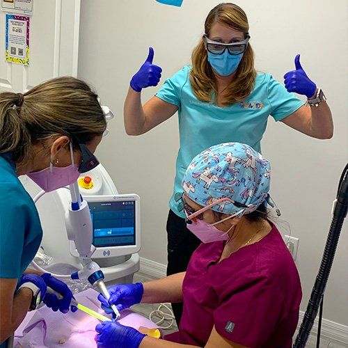 A group of nurses wearing masks and gloves are giving a thumbs up.