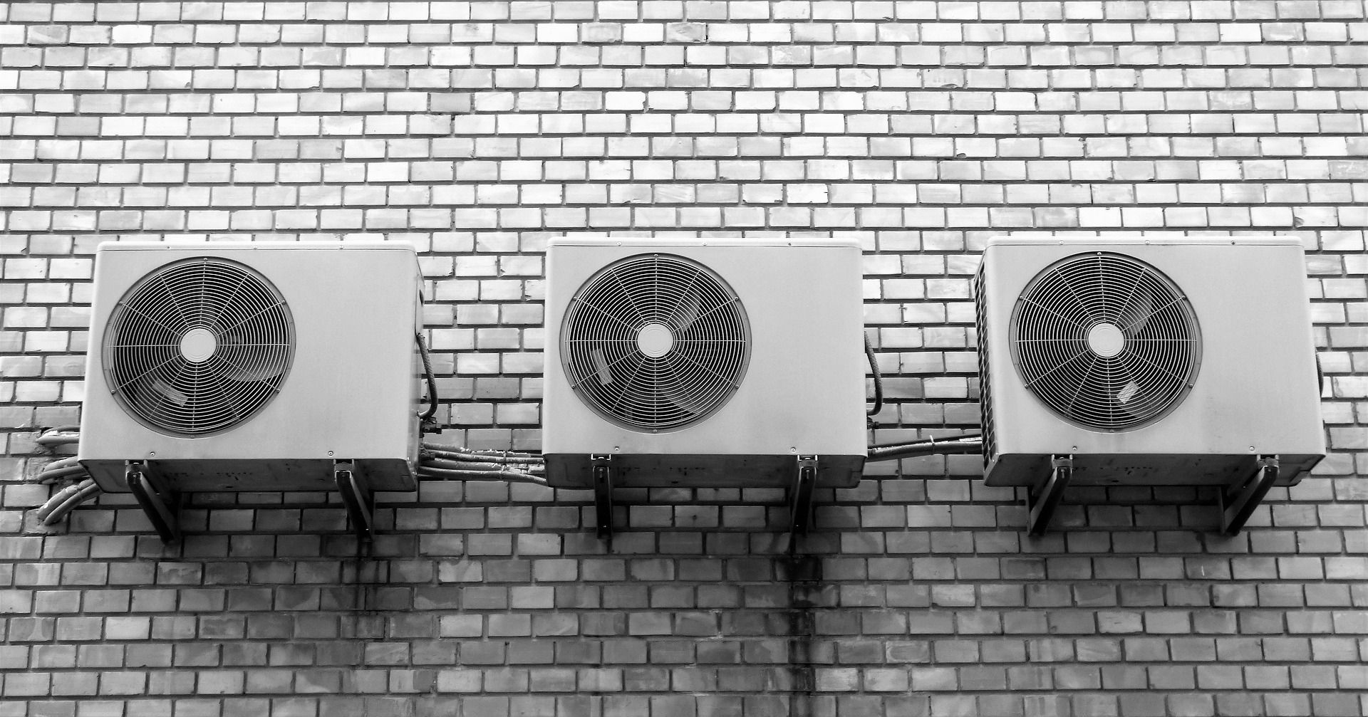 A black and white photo of three air conditioners mounted on a brick wall.