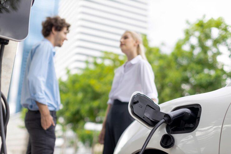 A man and a woman are standing next to an electric car that is being charged.