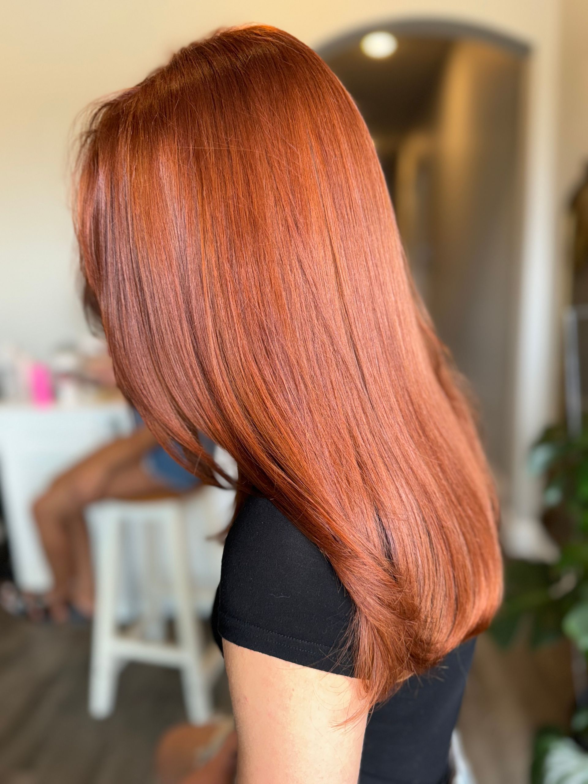 Long, straight, reddish-brown hair; person in a black shirt; indoor shot, blurred background.