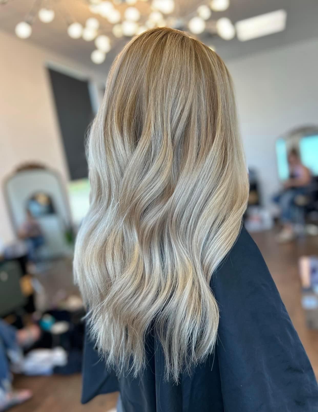 Blonde wavy hair styled in a salon setting, possibly a hair transformation with multiple blonde tones.
