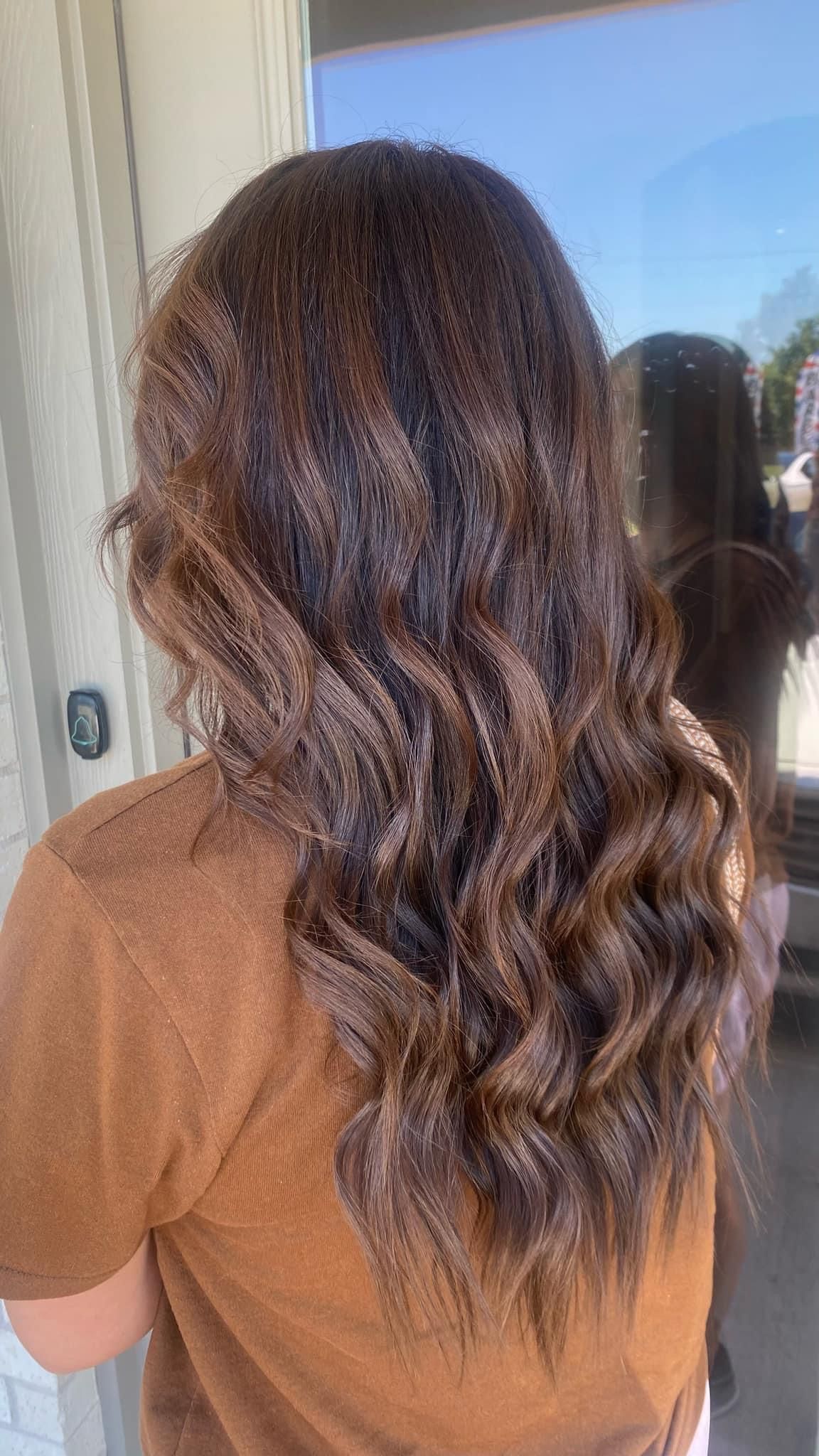 Woman with brown wavy hair and highlights, standing outside.