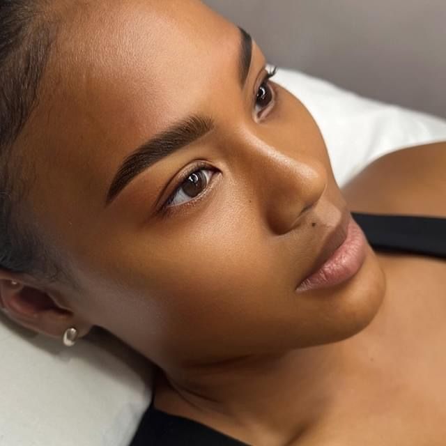 Woman with dark skin, perfect eyebrows and light makeup, resting on a white surface.