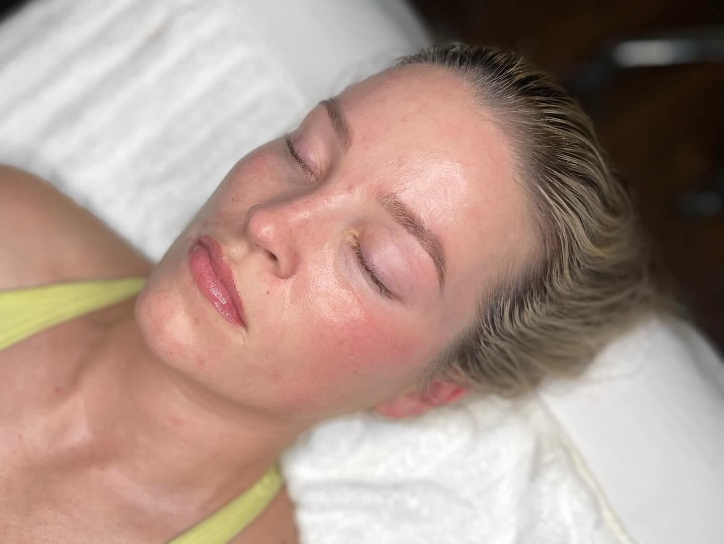 Woman with closed eyes, skin glows, lying on white surface, wearing light green top.