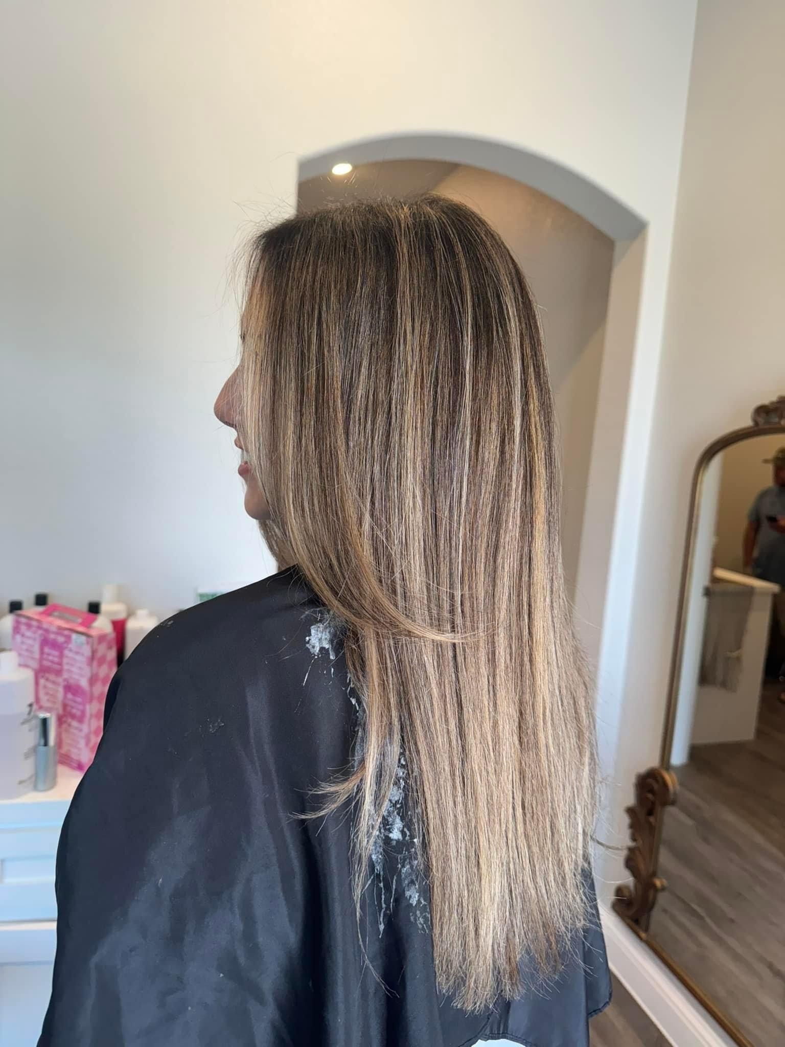 Person with long hair being styled at a salon. Hair is wet with highlights and covered by a black cape.
