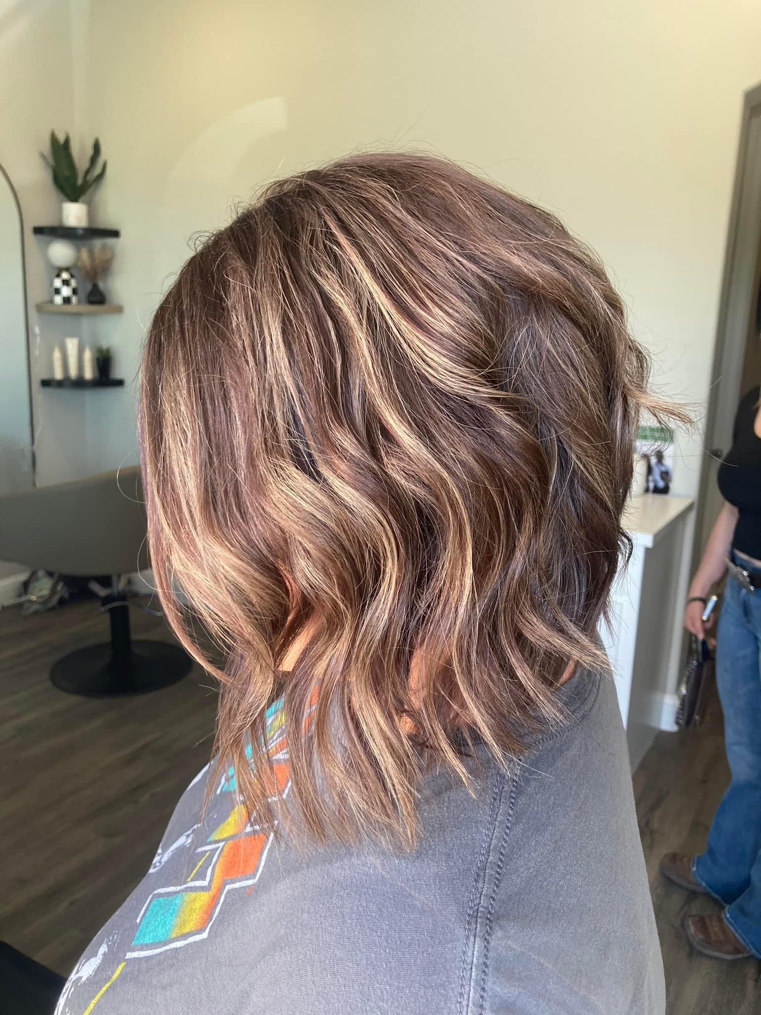 Woman with wavy, layered brown hair with blonde highlights at a salon.