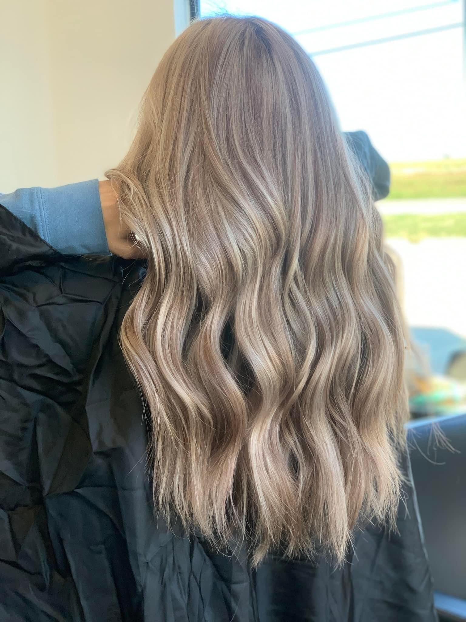 Long wavy light brown hair, styled in a salon, draped over a black cape.