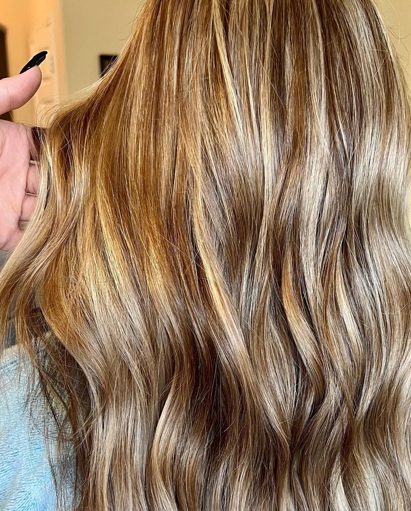 Wavy, highlighted hair in shades of brown and blonde. A hand gently holds a section of hair.