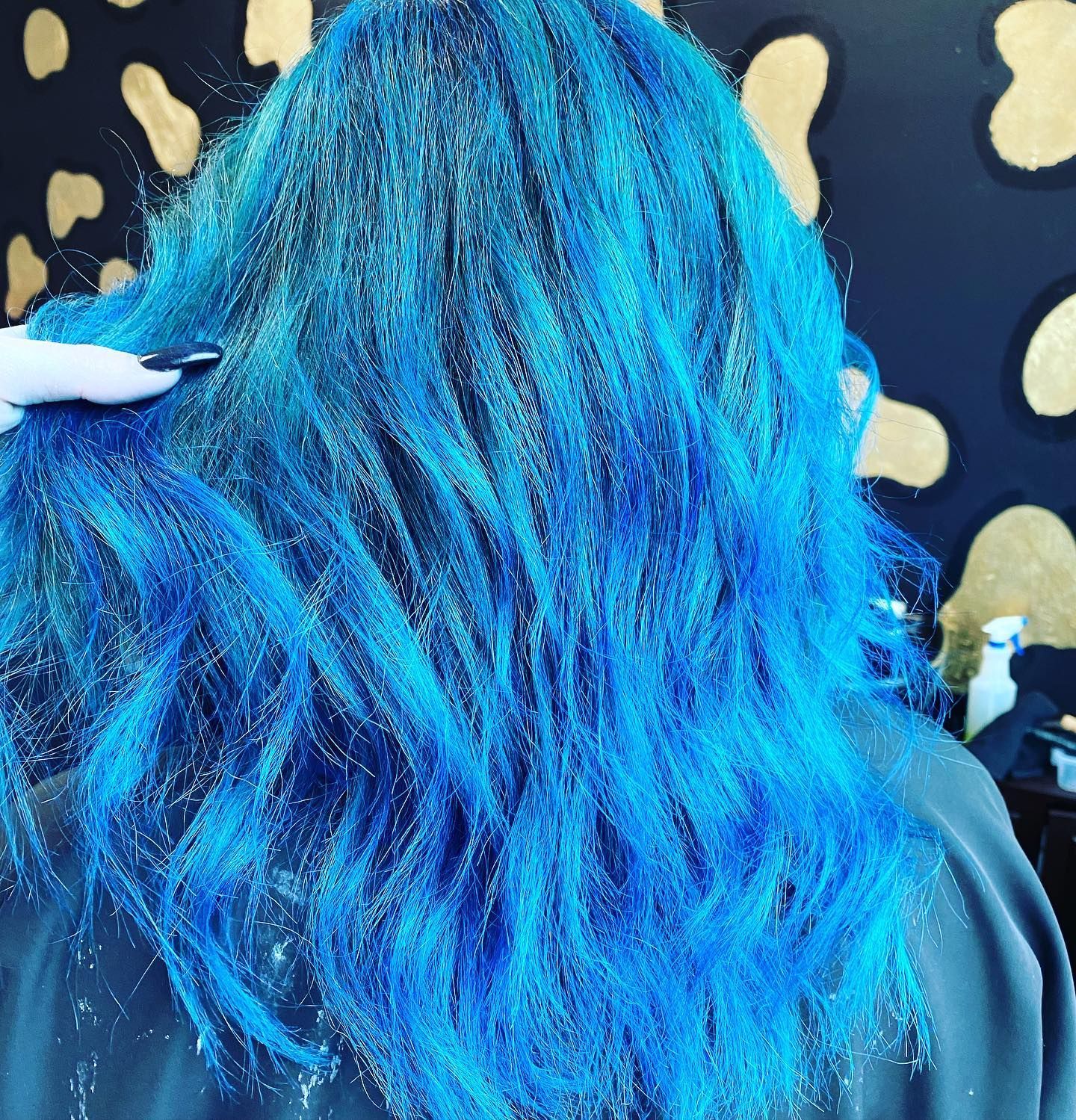Woman's hair dyed bright blue with long, wavy strands. She wears a black top, indoors.