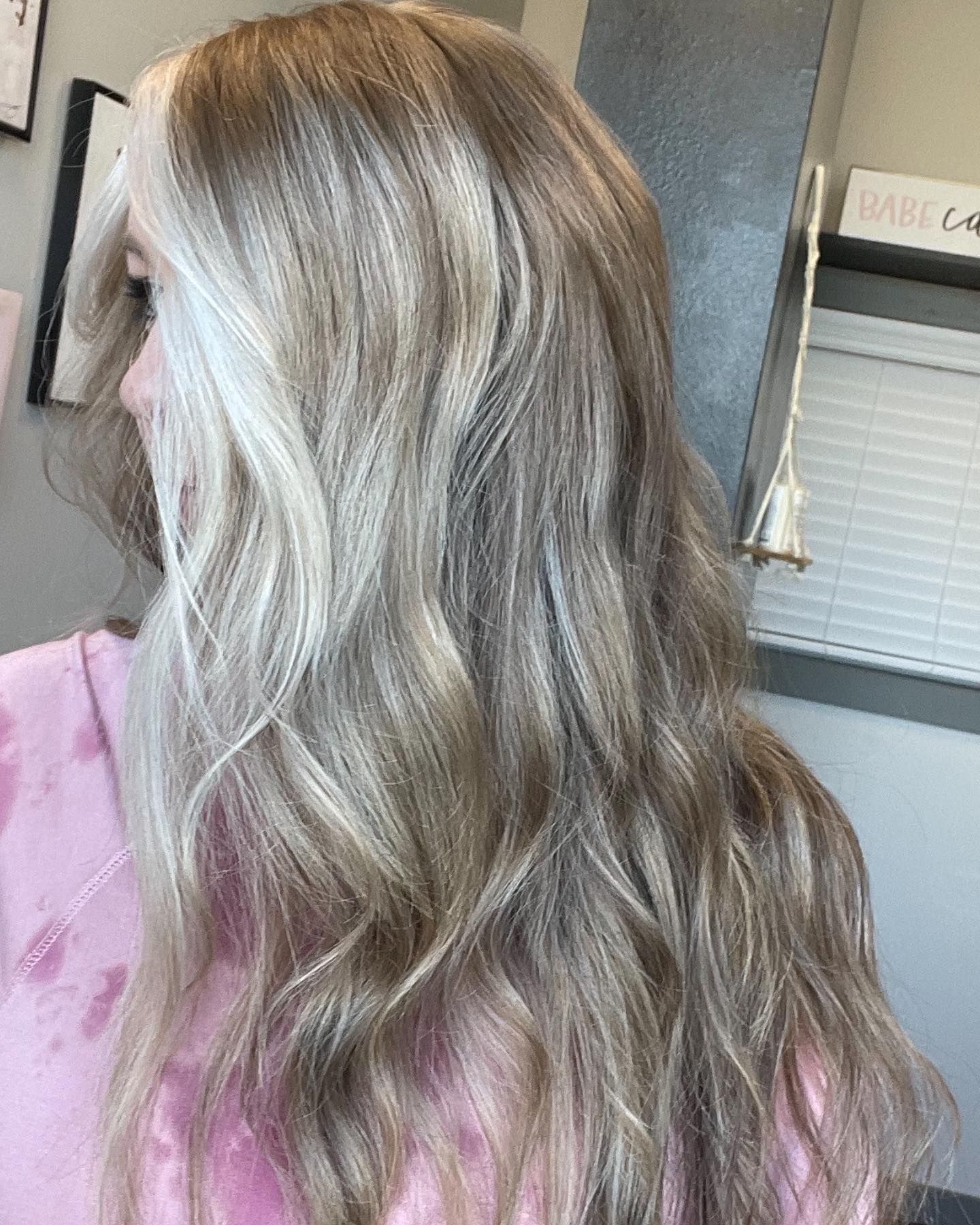 Woman with wavy blonde hair, wearing a pink shirt, indoors.