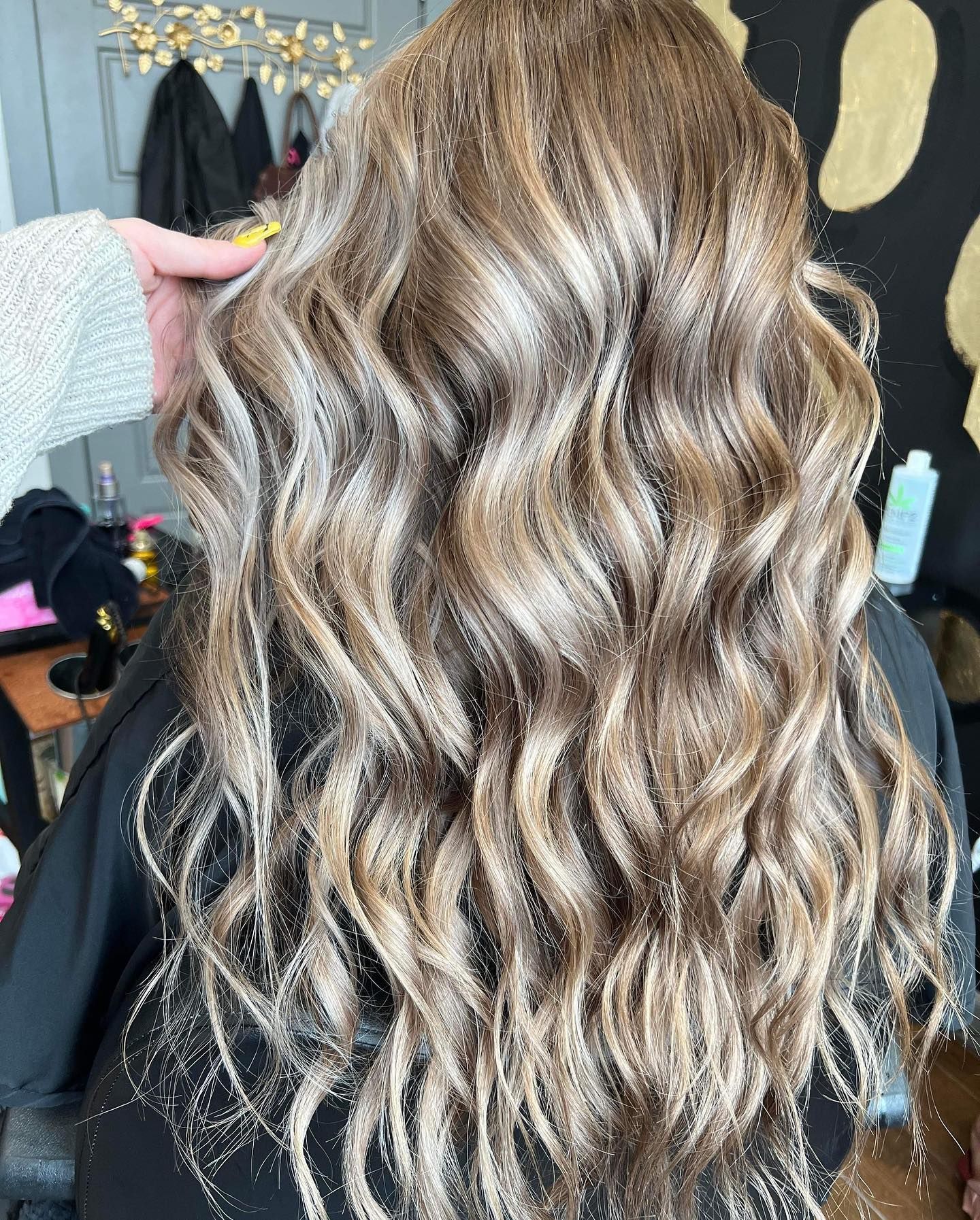 Long, wavy, light brown hair with highlights, styled in a salon, held by a hand.