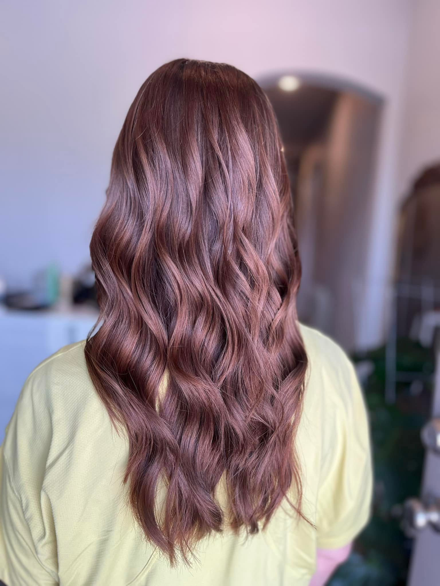 Woman with long, wavy, dark brown hair. She wears a yellow shirt, indoors.