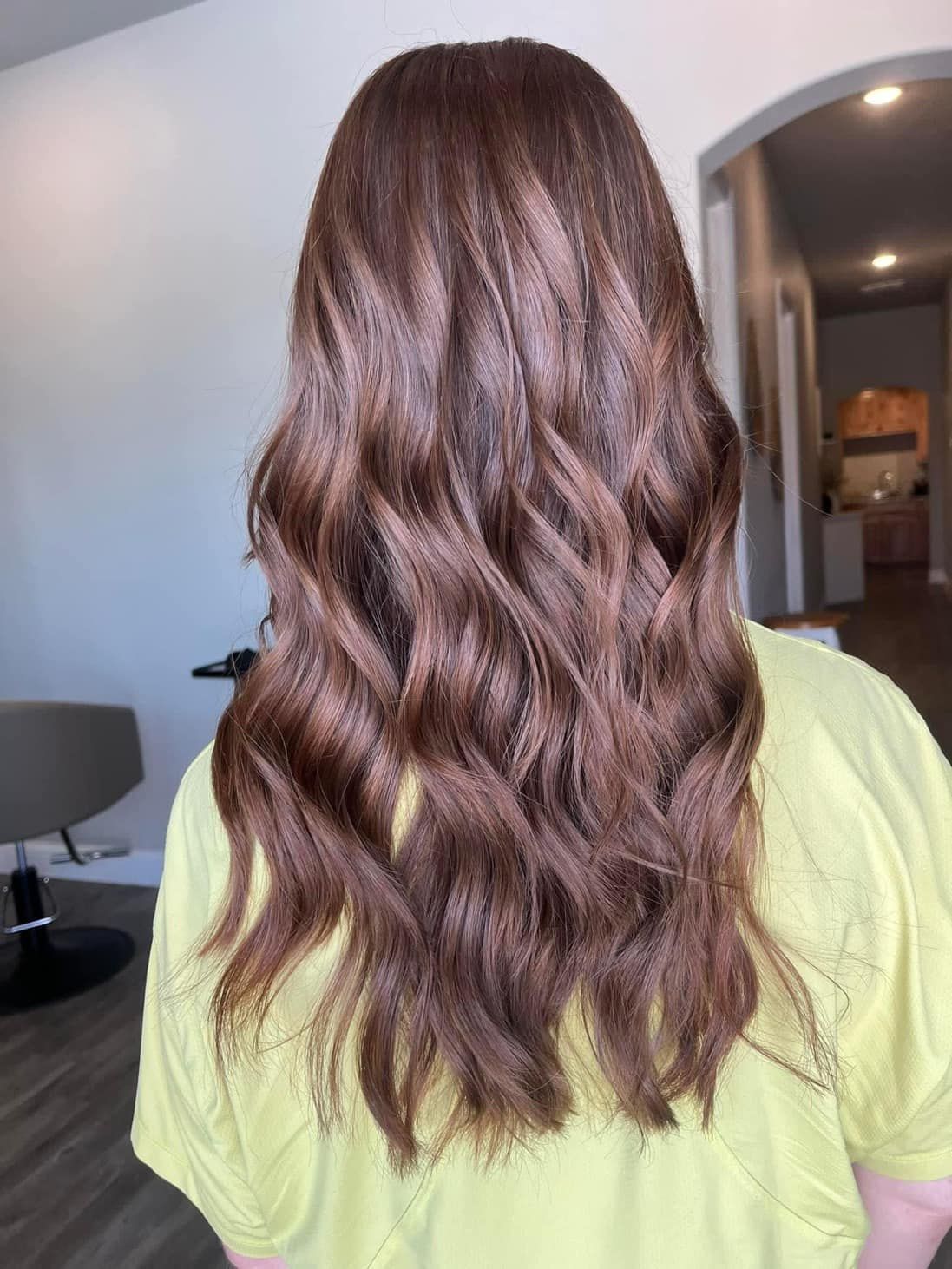Woman with long, wavy brown hair. She is wearing a yellow shirt, indoors.