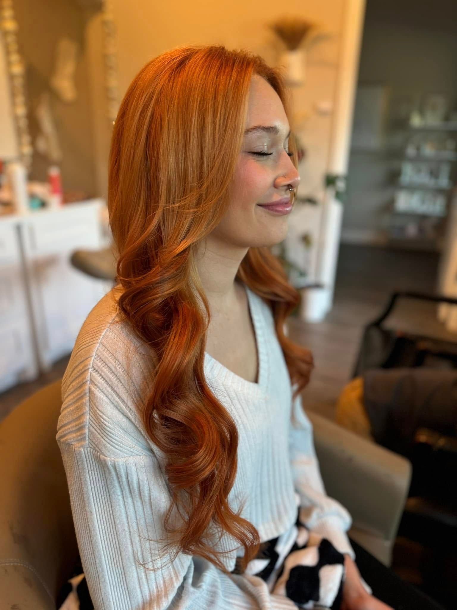 Woman with long, wavy auburn hair smiles with eyes closed. She wears a white sweater.