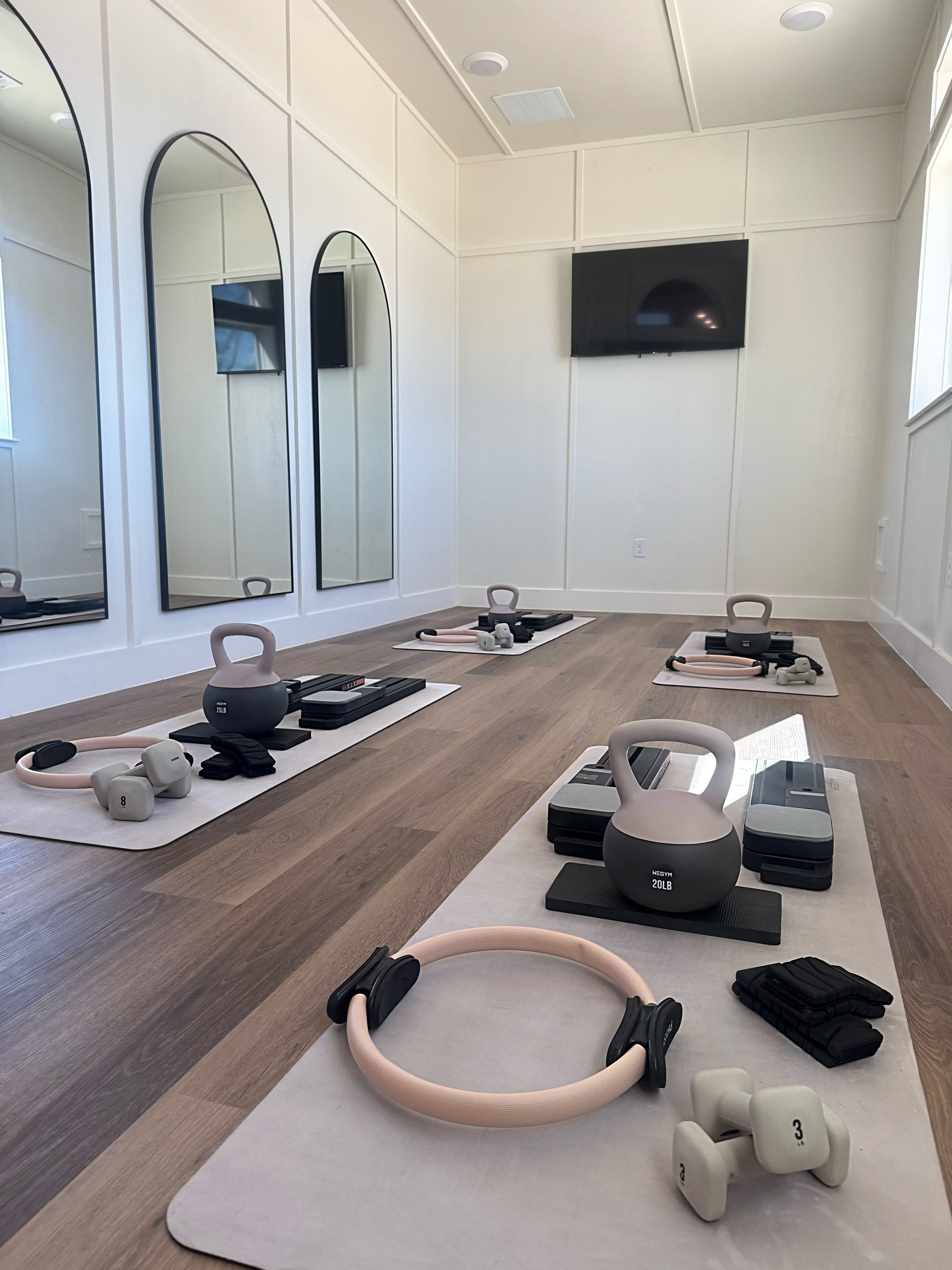 Workout studio with exercise equipment, including kettlebells, mats, and a TV. Mirrors line the walls.