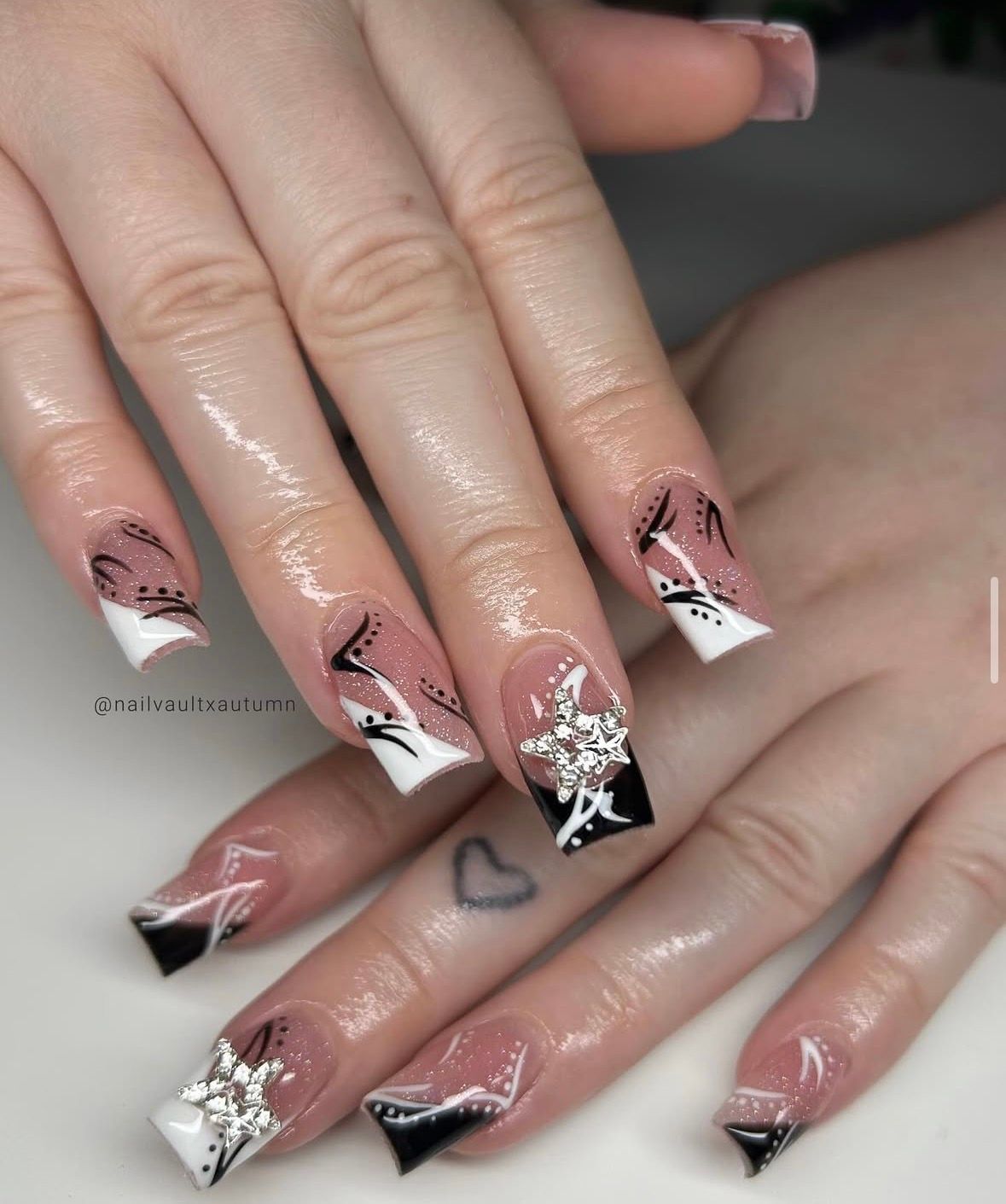 Hand with long, pink and clear acrylic nails. Some have black and white abstract designs.