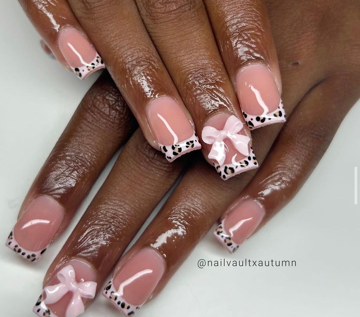 Close-up of manicured nails with pink tips, black and white animal print, and 3D pink bows.