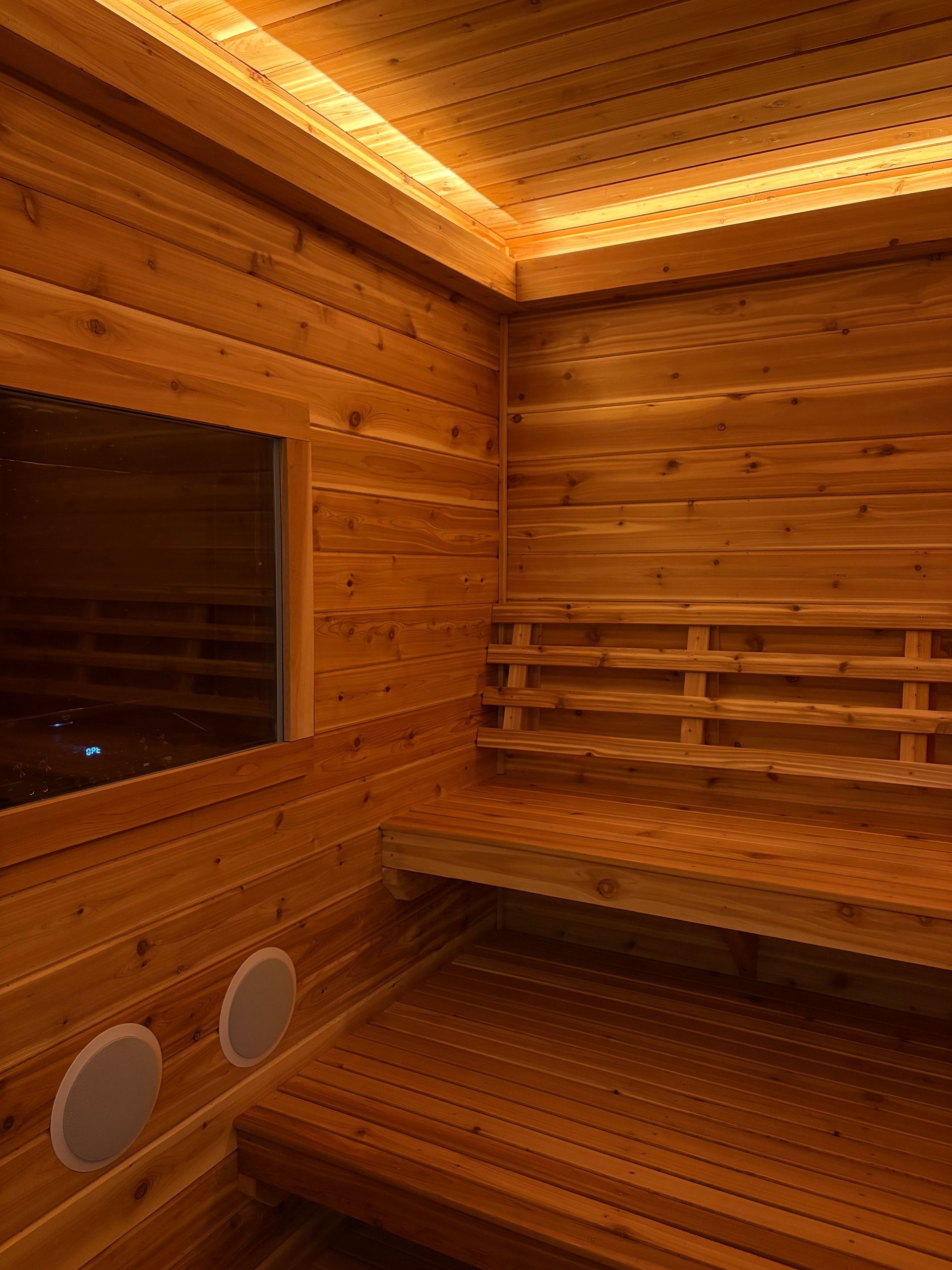 Wooden sauna interior with benches, window, and warm lighting.