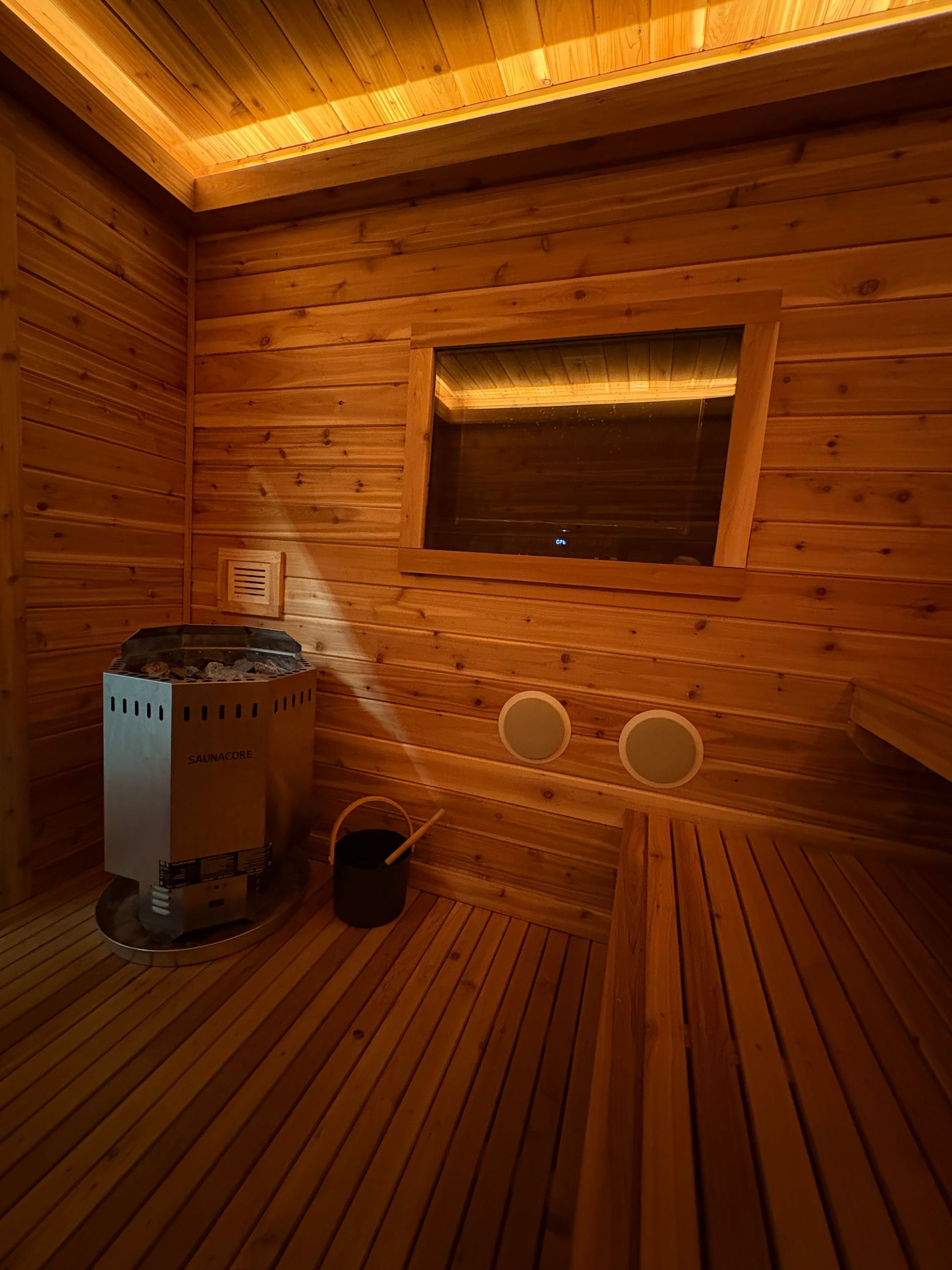 Wooden sauna interior with steam, towels, bucket, candles, and aroma bowl.