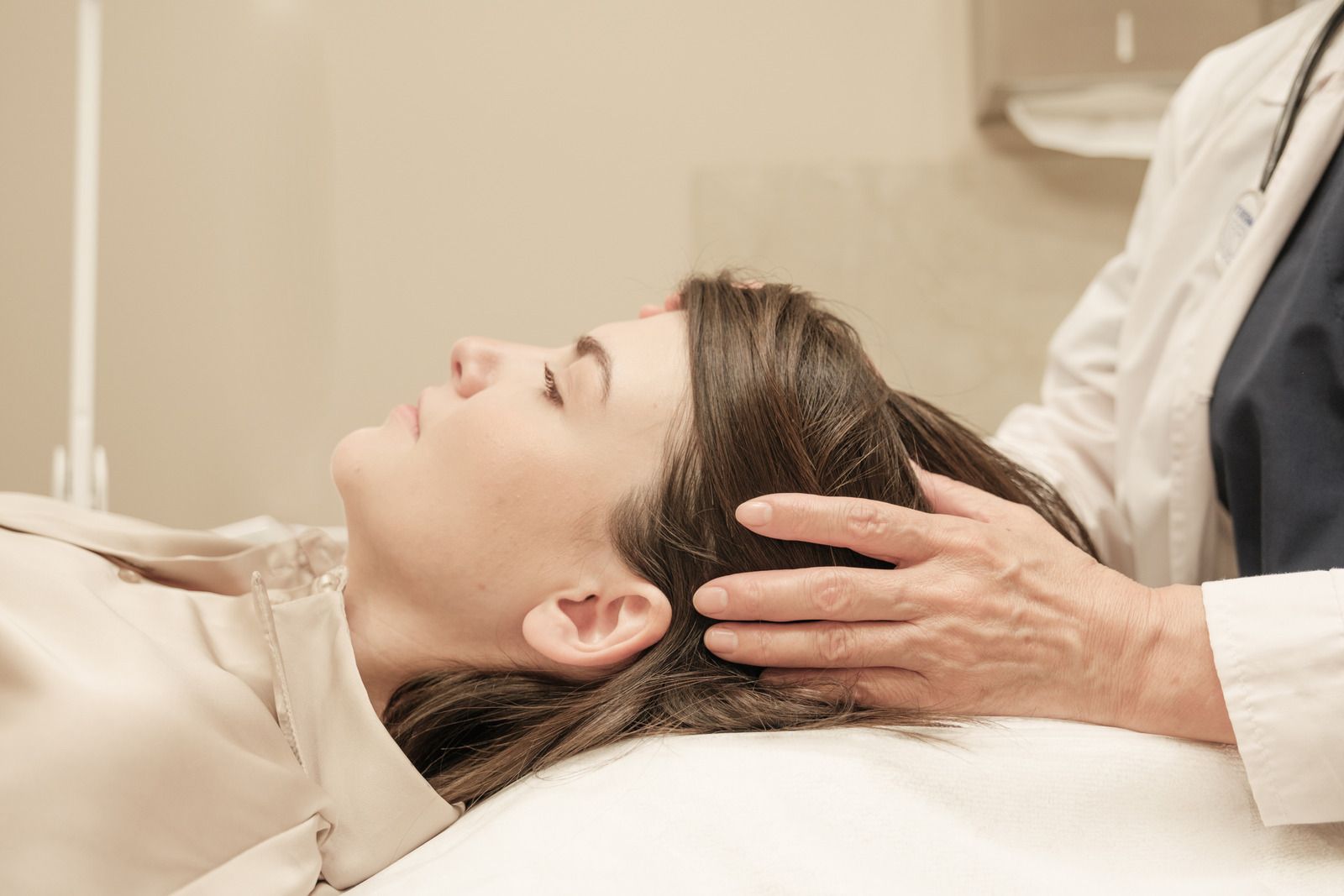 A practitioner gently holding the head of a person lying on a treatment table in a clinical or therapeutic setting.