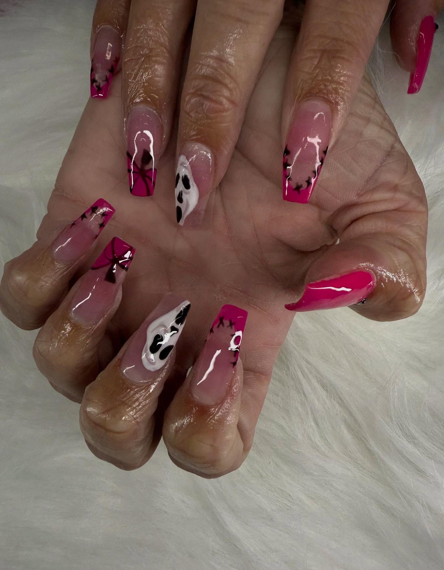 Hand with long, pink and clear acrylic nails. Some have black and white abstract designs.