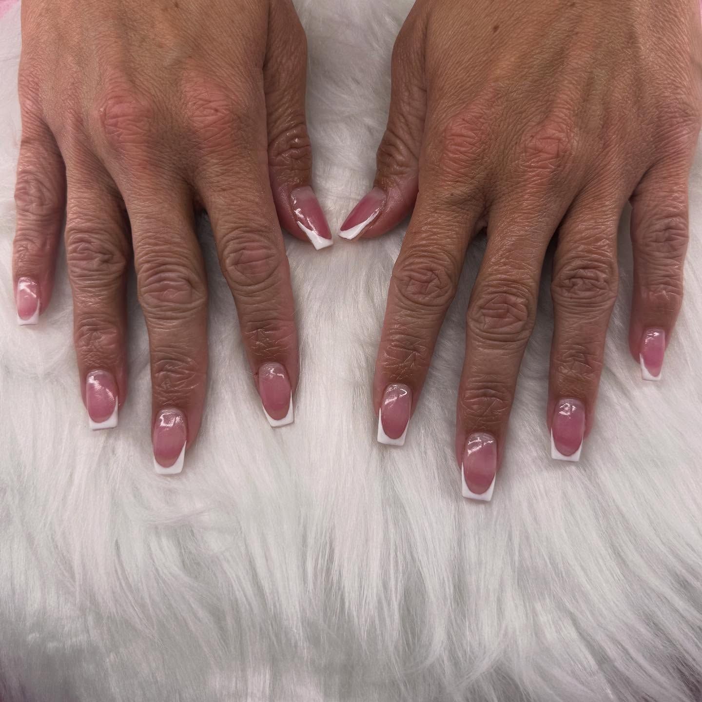 Hands with French tip nails, pink base and white tips.