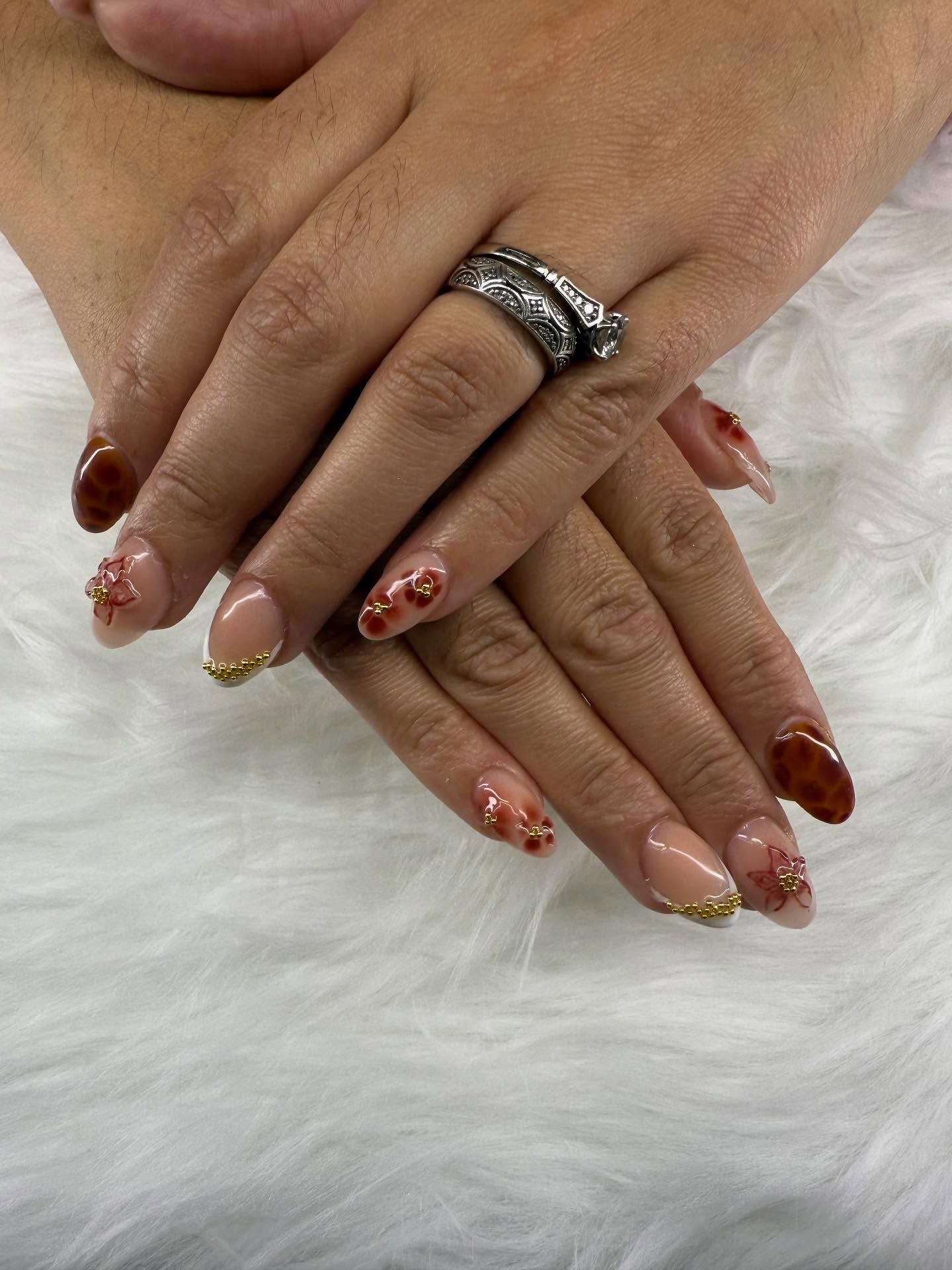 Hands with manicured nails, varying shades of brown, with gold accents and floral designs.