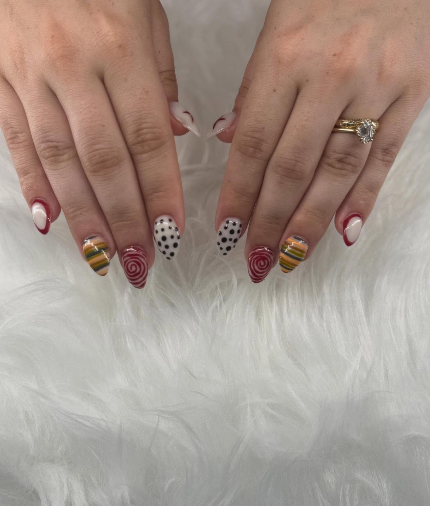 Hands with almond-shaped nails, featuring intricate designs in red, gold, black and white, against a fluffy white backdrop.