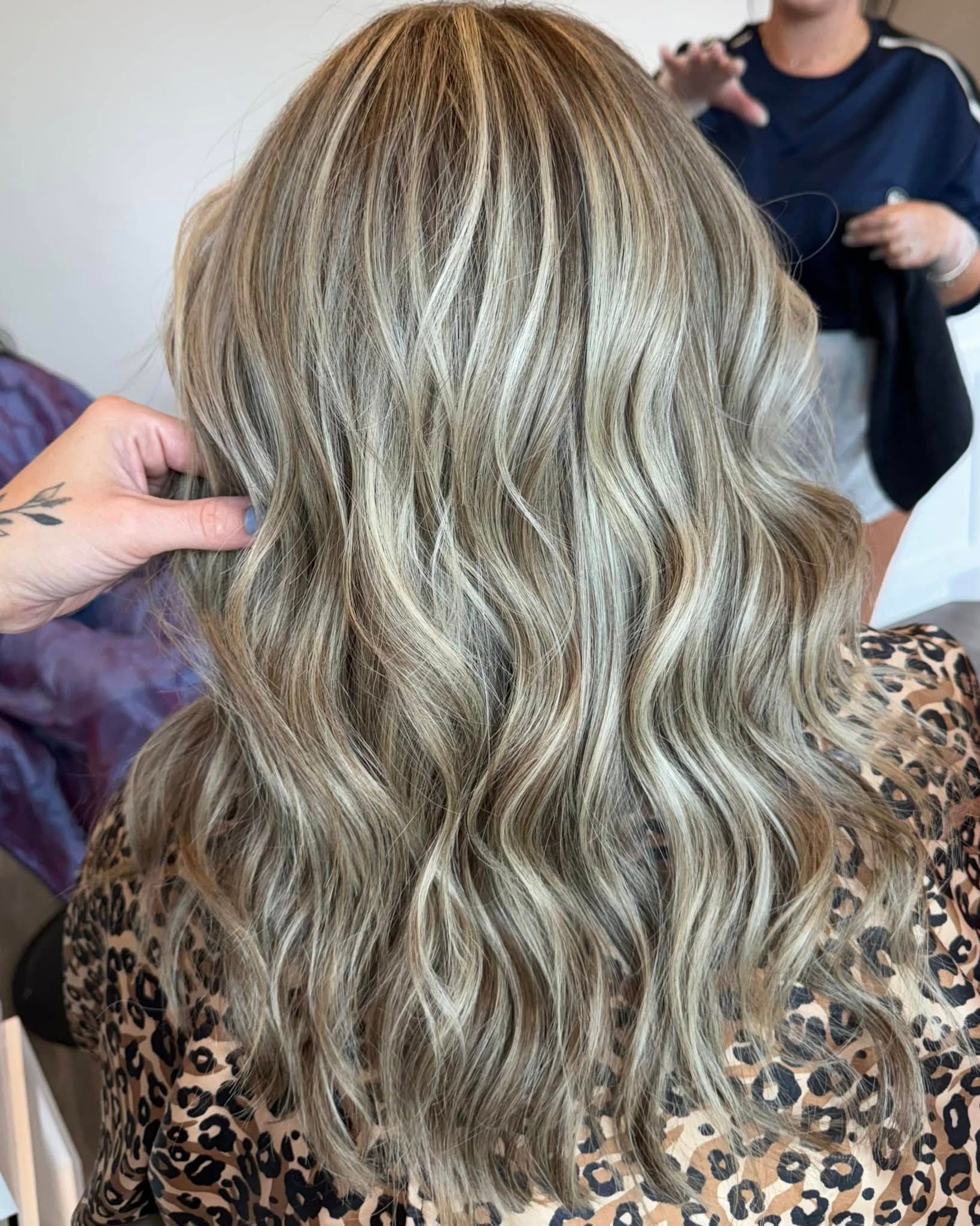 Woman's wavy highlighted hair styled in a salon, hands are adjusting the hair.